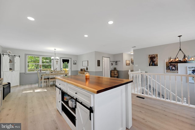 kitchen with a kitchen island, white cabinetry, decorative light fixtures, and light hardwood / wood-style flooring