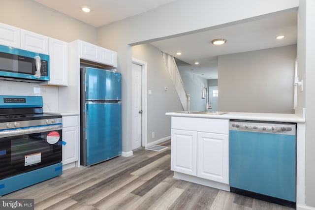 kitchen with light hardwood / wood-style floors, sink, stainless steel appliances, kitchen peninsula, and white cabinetry