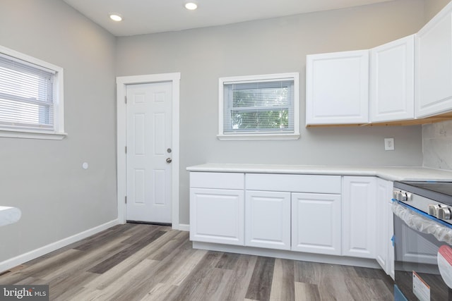 kitchen featuring stainless steel electric stove, light wood-type flooring, plenty of natural light, and white cabinets