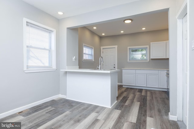 kitchen with kitchen peninsula, white cabinets, sink, and wood-type flooring