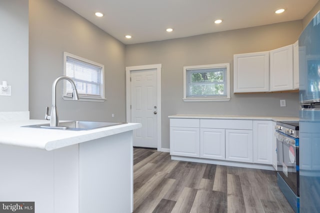 kitchen featuring sink, kitchen peninsula, white cabinetry, light hardwood / wood-style flooring, and electric range