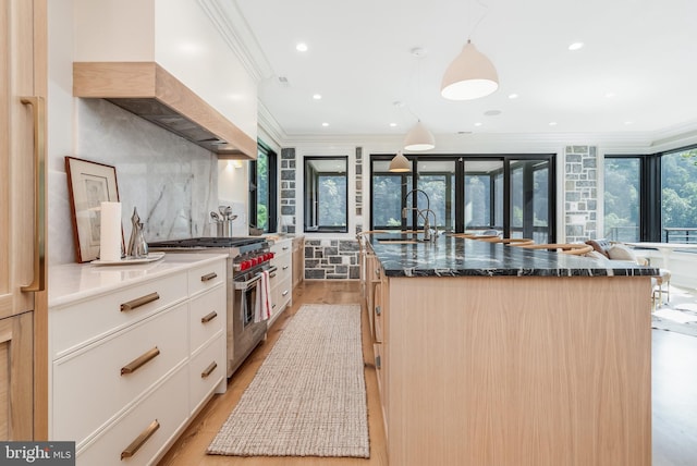 kitchen featuring white cabinets, light hardwood / wood-style flooring, a center island with sink, high end stainless steel range, and ornamental molding