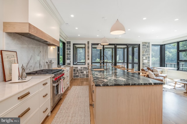 kitchen with high end range, sink, a large island with sink, and premium range hood