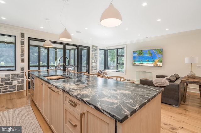 kitchen featuring sink, a center island with sink, decorative light fixtures, light hardwood / wood-style flooring, and light brown cabinetry