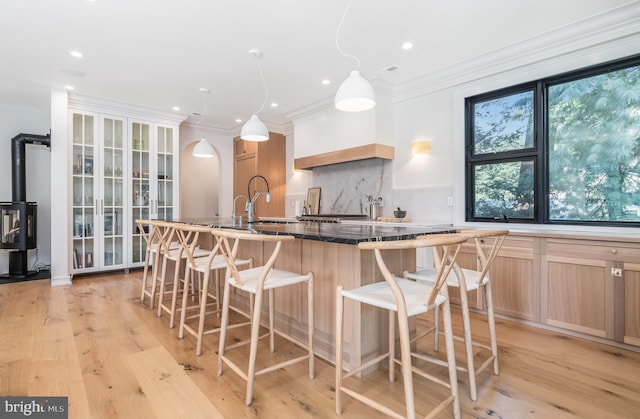 kitchen with a kitchen breakfast bar, backsplash, light wood-type flooring, crown molding, and light brown cabinetry