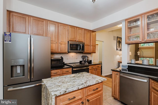 kitchen with a kitchen island, light stone countertops, backsplash, appliances with stainless steel finishes, and light tile patterned floors