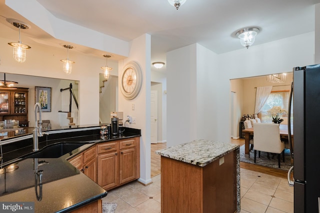 kitchen with light tile patterned flooring, decorative light fixtures, stainless steel refrigerator, a center island, and dark stone counters