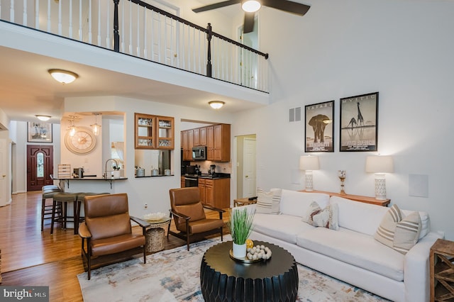 living room featuring a high ceiling, light hardwood / wood-style flooring, and ceiling fan