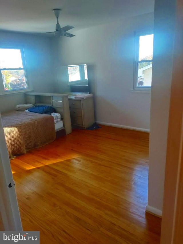 unfurnished bedroom featuring ceiling fan, multiple windows, and hardwood / wood-style flooring