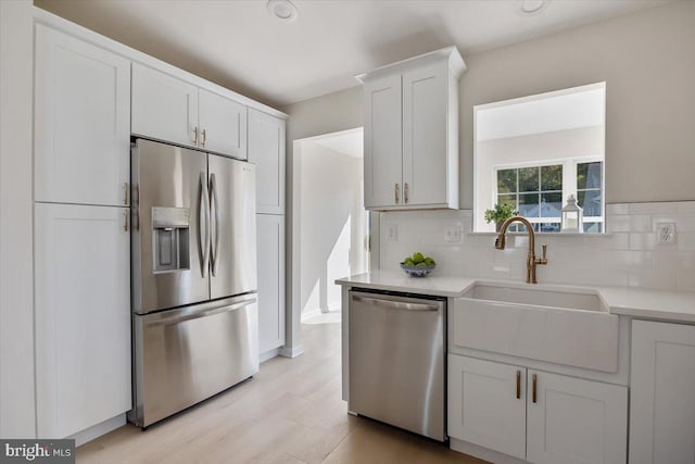 kitchen with light countertops, backsplash, stainless steel appliances, light wood finished floors, and a sink