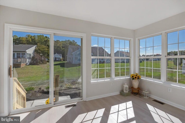 unfurnished sunroom featuring wood finished floors, baseboards, visible vents, and plenty of natural light