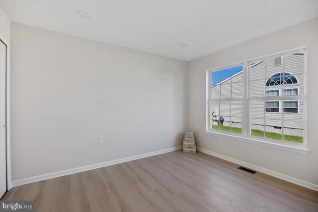 empty room featuring wood finished floors, baseboards, and visible vents