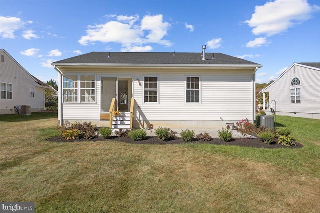 rear view of house with central AC unit, entry steps, and a lawn