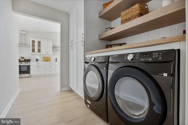 clothes washing area with washer and clothes dryer, cabinets, and light hardwood / wood-style floors