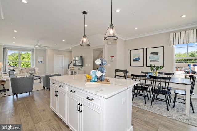 kitchen featuring white cabinetry, light stone counters, pendant lighting, light wood-type flooring, and a center island