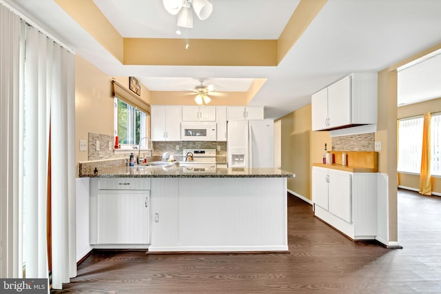 kitchen with white cabinets, dark stone countertops, white appliances, sink, and dark hardwood / wood-style flooring