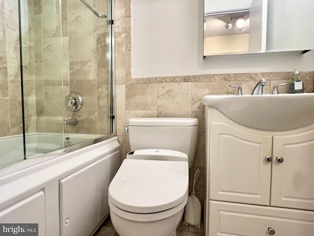 full bathroom featuring shower / bath combination with glass door, vanity, toilet, and tile walls