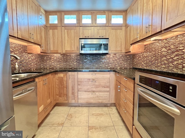 kitchen with backsplash, dark stone countertops, light tile patterned floors, and stainless steel appliances