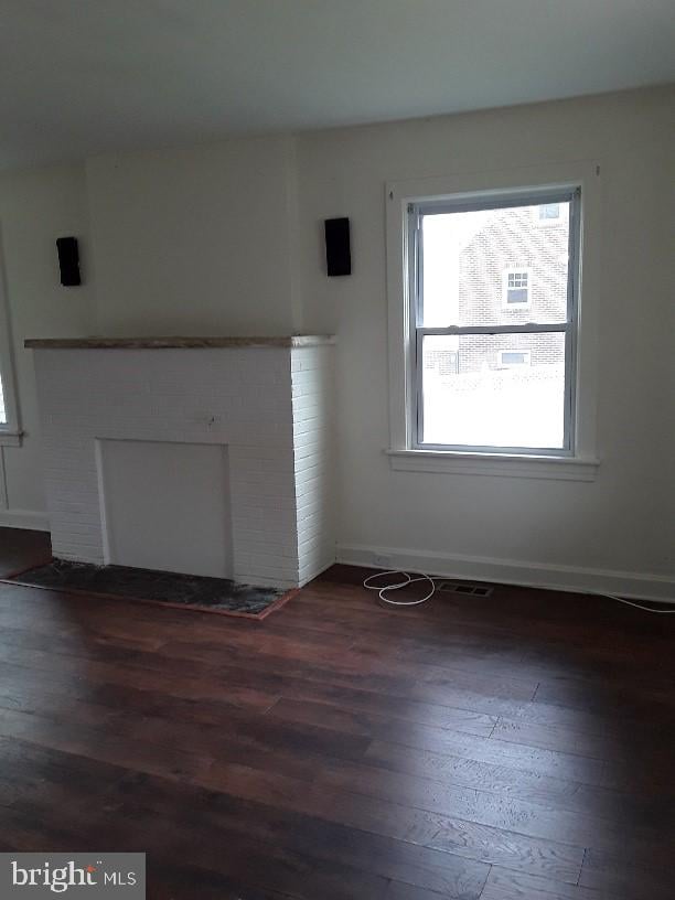 unfurnished living room with dark wood-type flooring and a brick fireplace