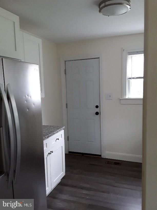 kitchen with white cabinets, light stone countertops, stainless steel fridge, and dark hardwood / wood-style flooring