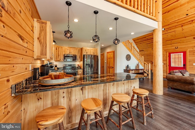 kitchen with kitchen peninsula, appliances with stainless steel finishes, light brown cabinetry, decorative light fixtures, and wood walls