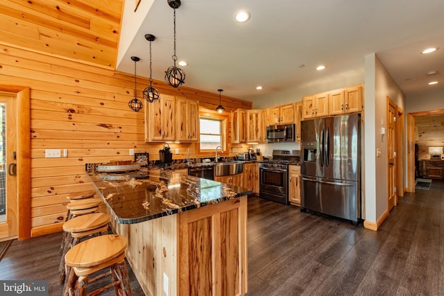 kitchen featuring kitchen peninsula, wooden walls, hanging light fixtures, and stainless steel appliances