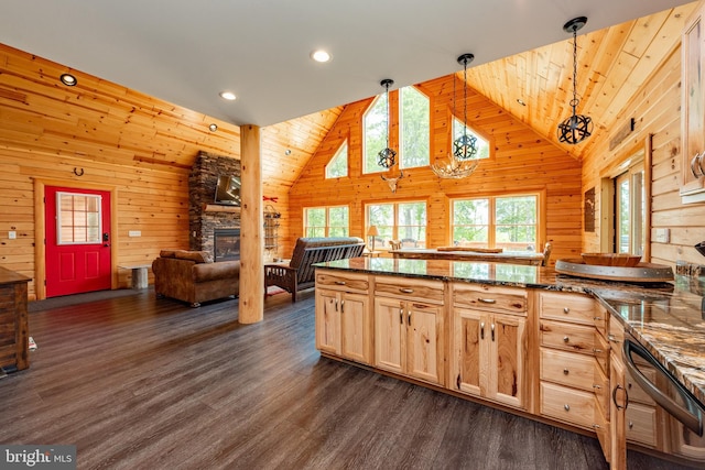 kitchen featuring a stone fireplace, wood walls, light brown cabinetry, and pendant lighting