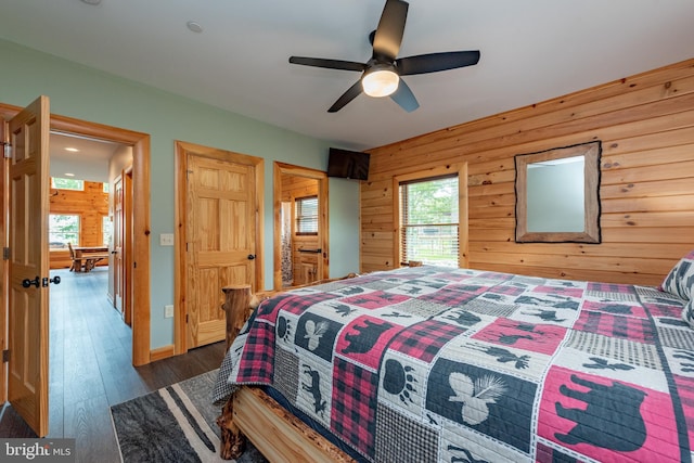 bedroom with multiple windows, wood walls, ceiling fan, and dark hardwood / wood-style floors