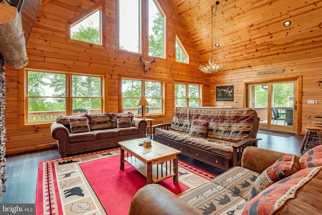 living room featuring high vaulted ceiling, an inviting chandelier, wooden walls, dark hardwood / wood-style floors, and a wealth of natural light