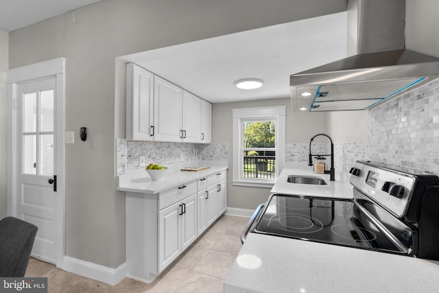 kitchen with wall chimney range hood, light tile patterned floors, white cabinetry, range with electric cooktop, and sink