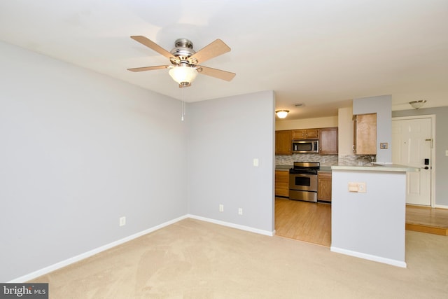 kitchen with light carpet, kitchen peninsula, stainless steel appliances, tasteful backsplash, and ceiling fan