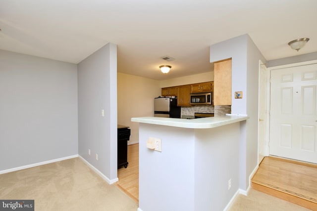 kitchen with backsplash, stainless steel appliances, light carpet, and kitchen peninsula