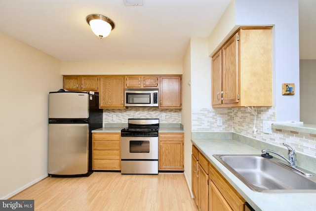 kitchen with tasteful backsplash, appliances with stainless steel finishes, sink, and light wood-type flooring