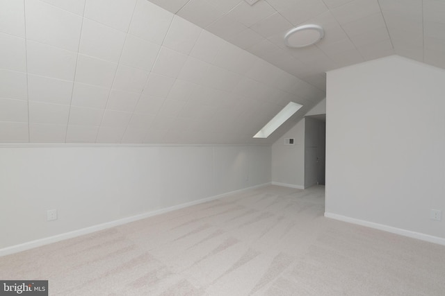 additional living space with vaulted ceiling with skylight and light colored carpet