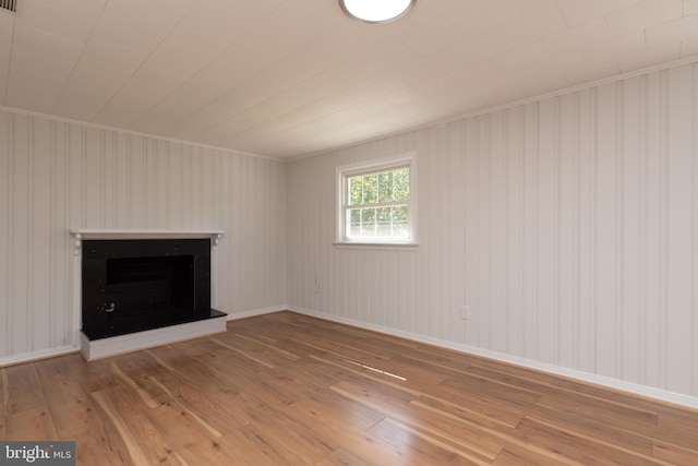 unfurnished living room featuring crown molding, wood walls, and hardwood / wood-style floors