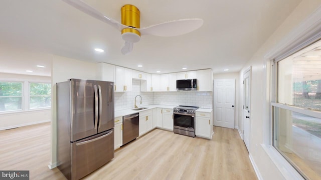 kitchen featuring stainless steel appliances, sink, white cabinets, light hardwood / wood-style floors, and tasteful backsplash