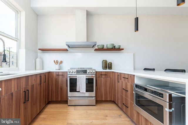 kitchen featuring light wood-type flooring, sink, extractor fan, appliances with stainless steel finishes, and decorative light fixtures