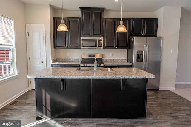 kitchen featuring appliances with stainless steel finishes, hanging light fixtures, a kitchen island with sink, and sink