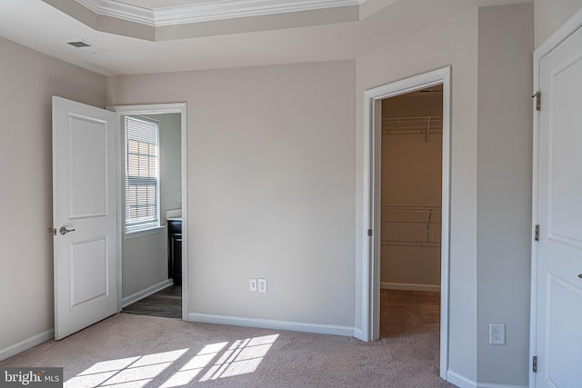 unfurnished bedroom with a closet, ornamental molding, light colored carpet, and a walk in closet