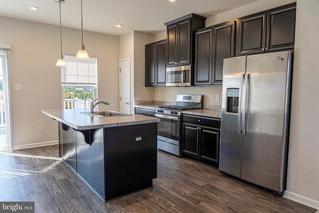 kitchen with a kitchen island with sink, dark hardwood / wood-style floors, sink, hanging light fixtures, and appliances with stainless steel finishes