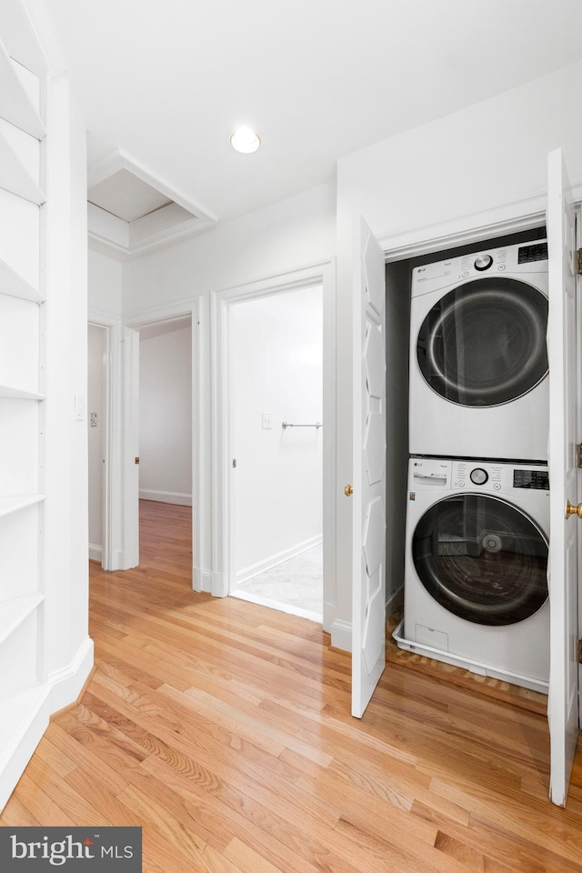 laundry area featuring stacked washing maching and dryer and light hardwood / wood-style flooring