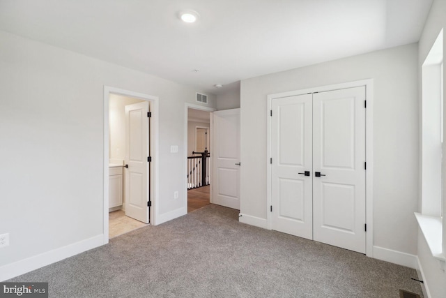 unfurnished bedroom featuring light colored carpet, a closet, and ensuite bath