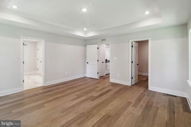 unfurnished bedroom featuring hardwood / wood-style flooring, crown molding, a tray ceiling, and ensuite bath