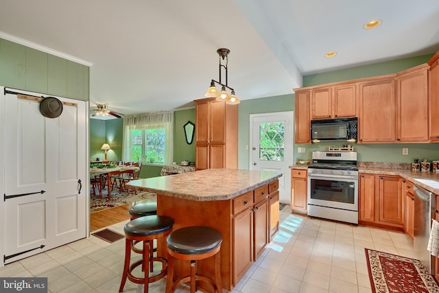 kitchen with ceiling fan, a kitchen breakfast bar, hanging light fixtures, appliances with stainless steel finishes, and a center island