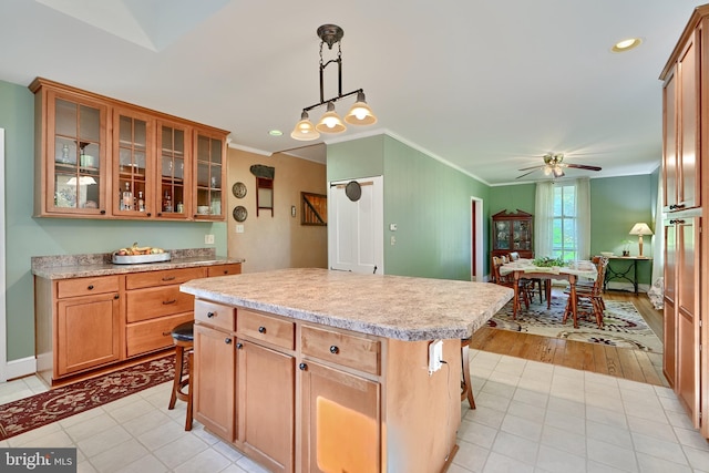 kitchen with ceiling fan, hanging light fixtures, a kitchen island, light hardwood / wood-style flooring, and a kitchen bar