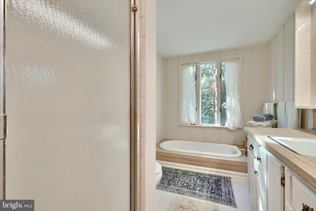 bathroom with tile patterned floors, toilet, vanity, and tiled bath