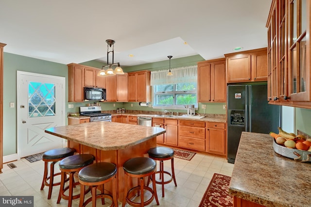 kitchen with a breakfast bar area, decorative light fixtures, sink, black appliances, and a center island