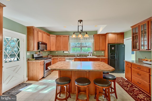 kitchen with decorative light fixtures, black appliances, a kitchen island, and a wealth of natural light