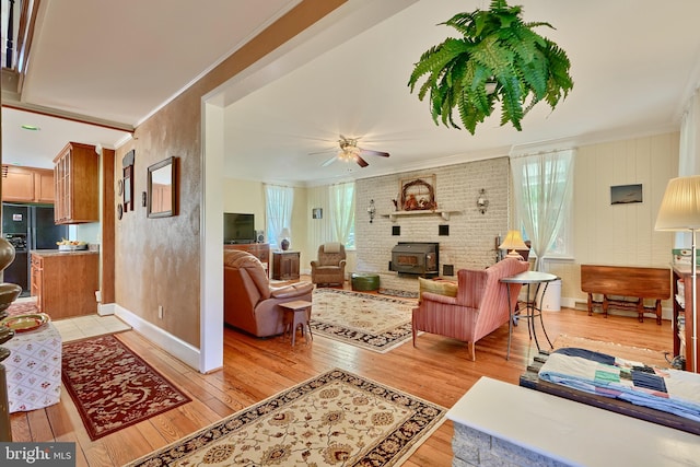 living room with ceiling fan, crown molding, light hardwood / wood-style floors, and a wood stove