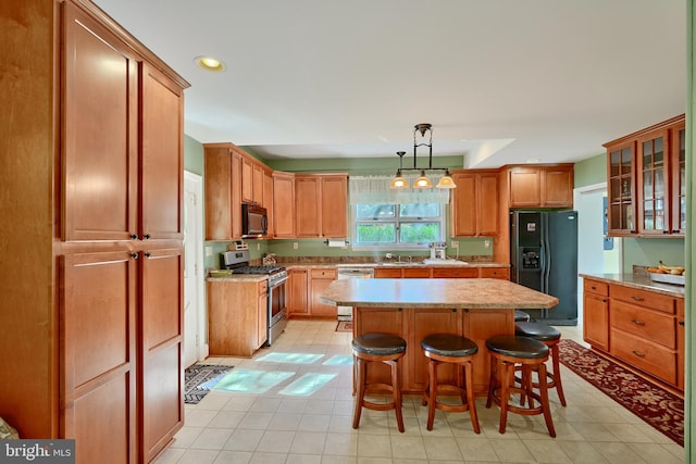 kitchen with a kitchen island, black appliances, light tile patterned flooring, pendant lighting, and a kitchen bar